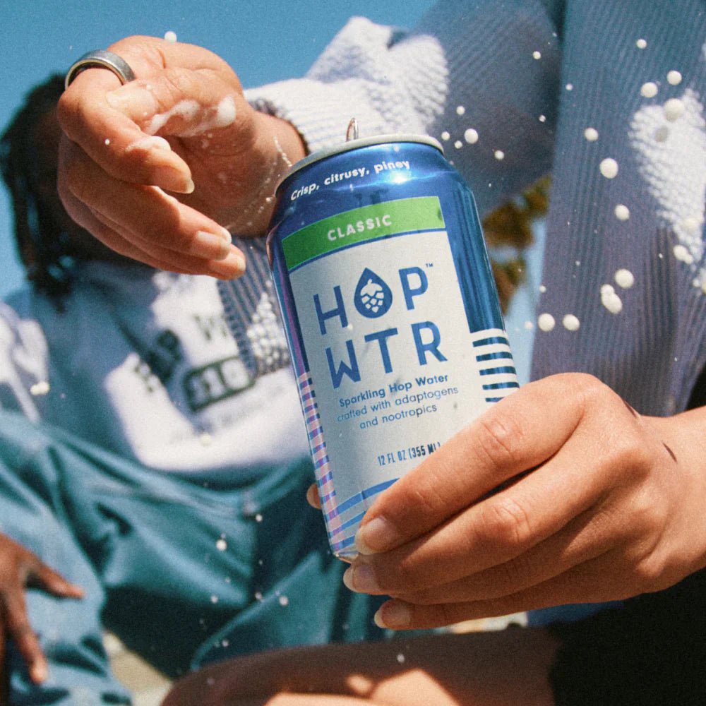 Person holding a HOPWTR Classic can with water splashing around it