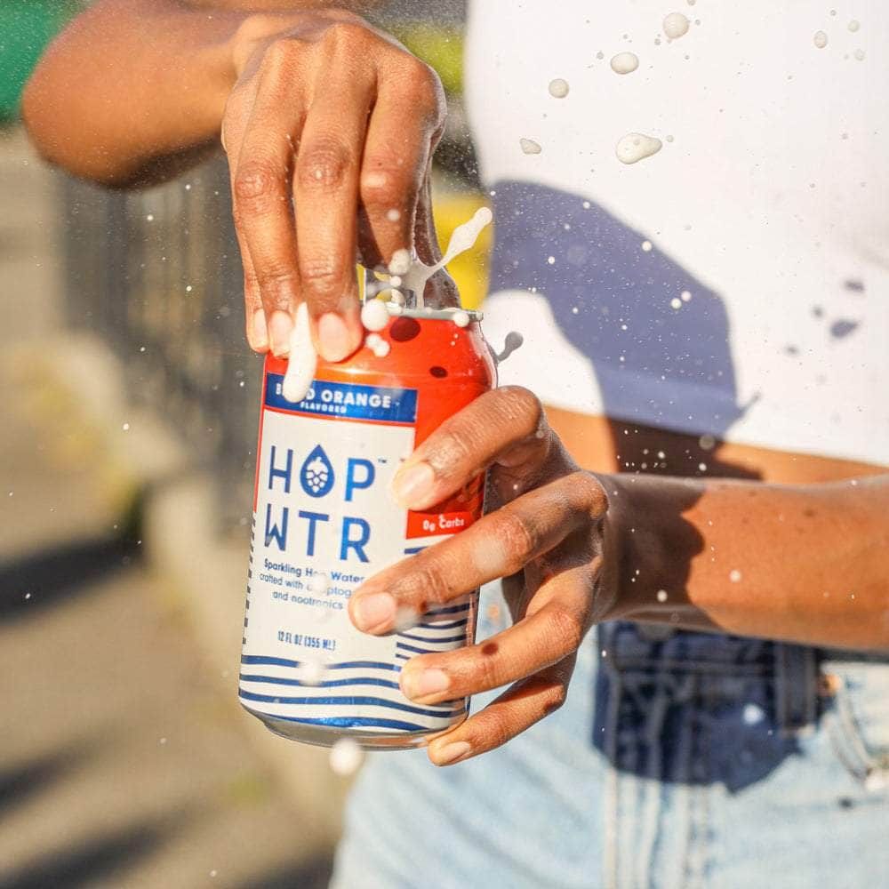Hands opening a HOPWTR Blood Orange can with a splash